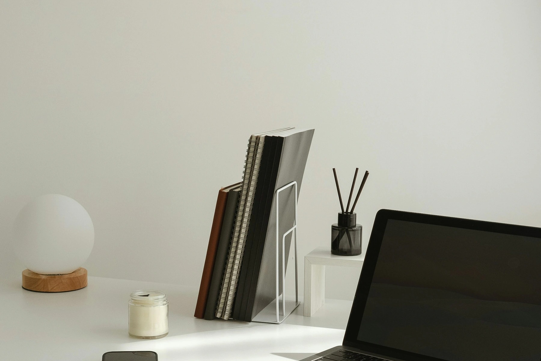 A simple desk with a laptop, notebooks and a round lamp