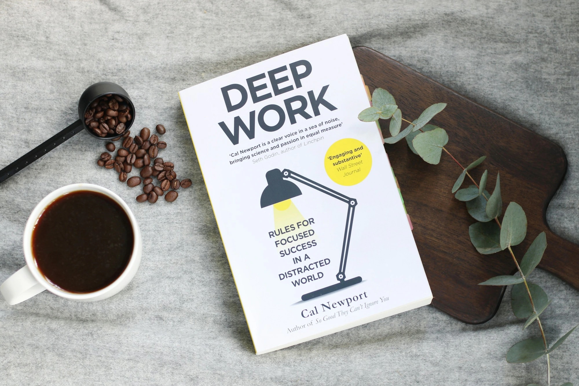 Cal Newport’s Deep Work book beside a cup of coffee, coffee beans and eucalyptus leaves