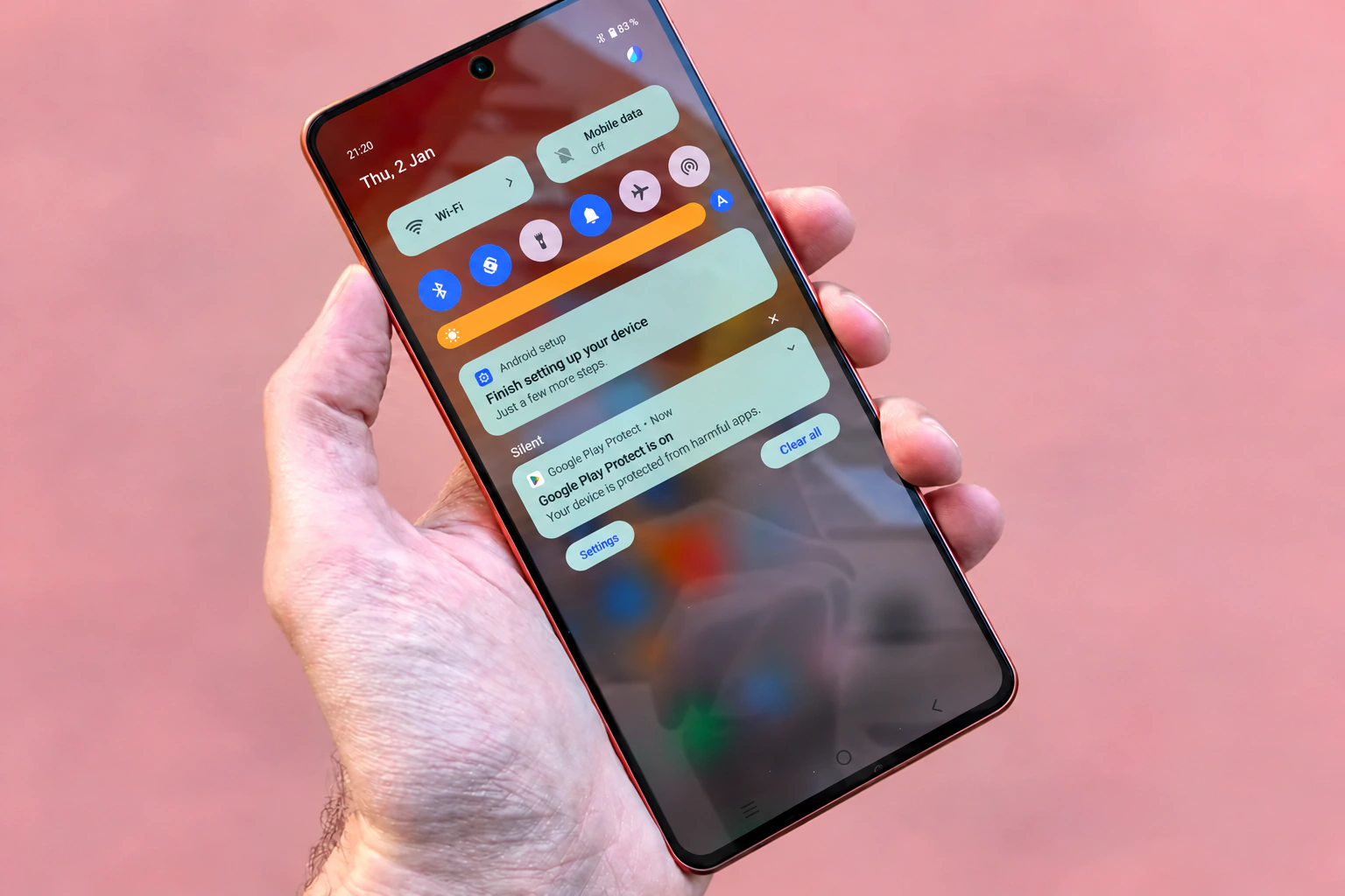 A hand holding a phone with British English notifications and mint control tiles