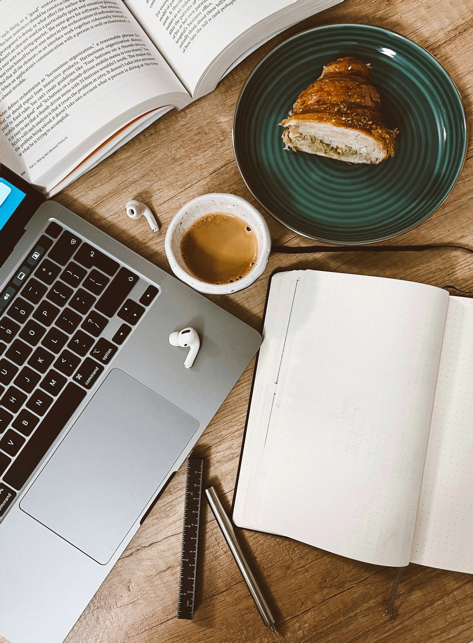 An open notebook, laptop and earphones on a wooden table