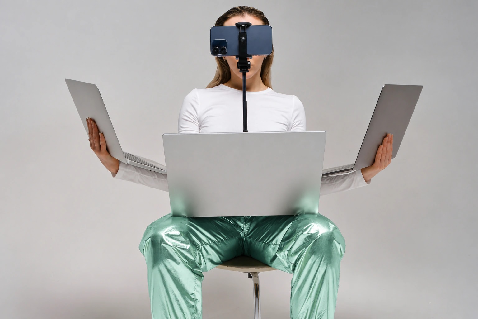 A seated person in a white shirt and mint green trousers with three laptops and a mounted phone