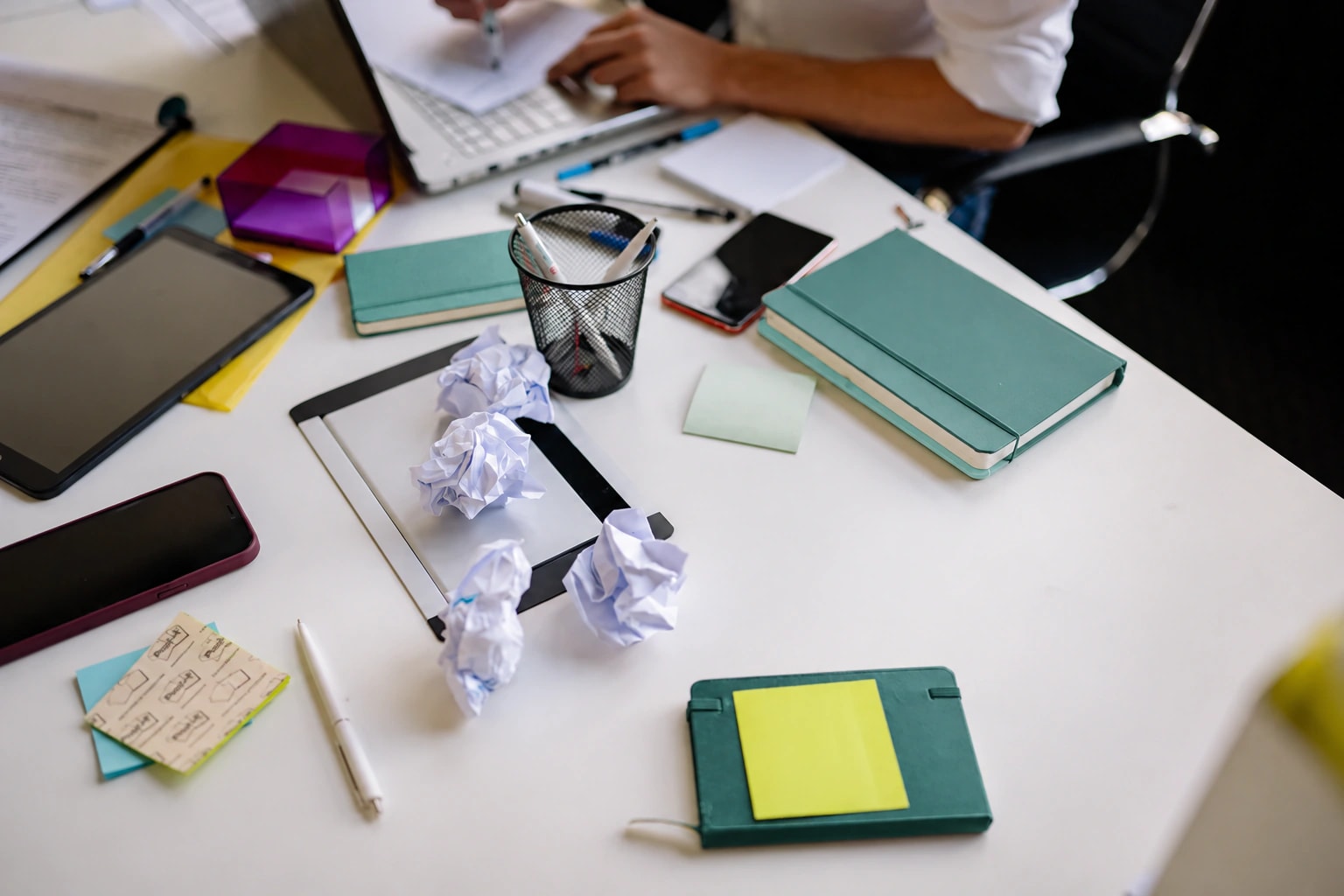 Crumpled papers, green and mint notebooks and sticky notes spread across a shared desk