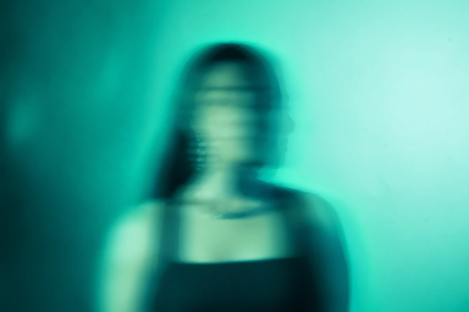 A motion-blurred portrait with overlapping profiles in vivid teal and mint light