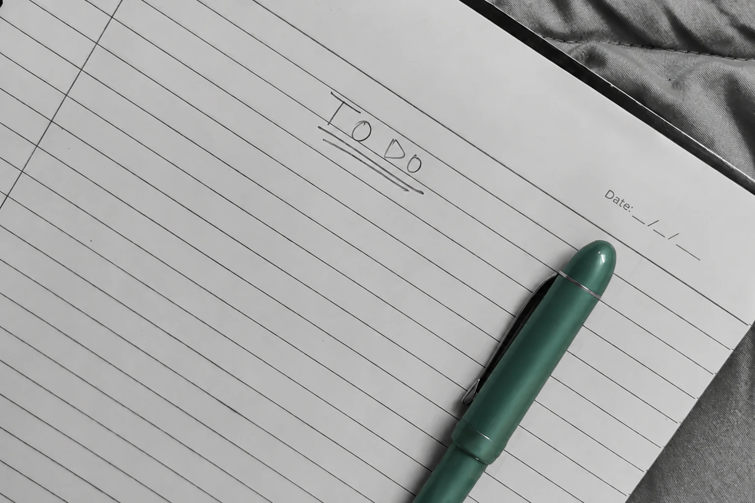 A green pen lying diagonally across a monochrome notebook headed To Do